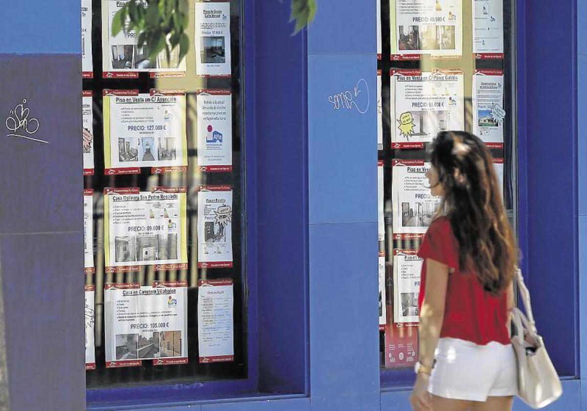 Una joven mira un escaparte con anuncios de pisos en alquiler.