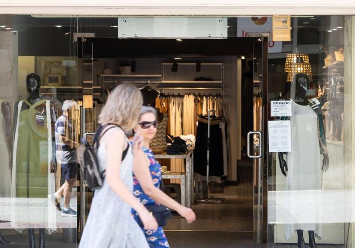 Dos mujeres caminan por delante de un comercio.