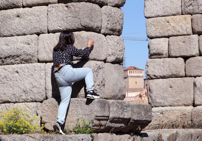 Una mujer, encaramada a uno de los sillares del Acueducto.