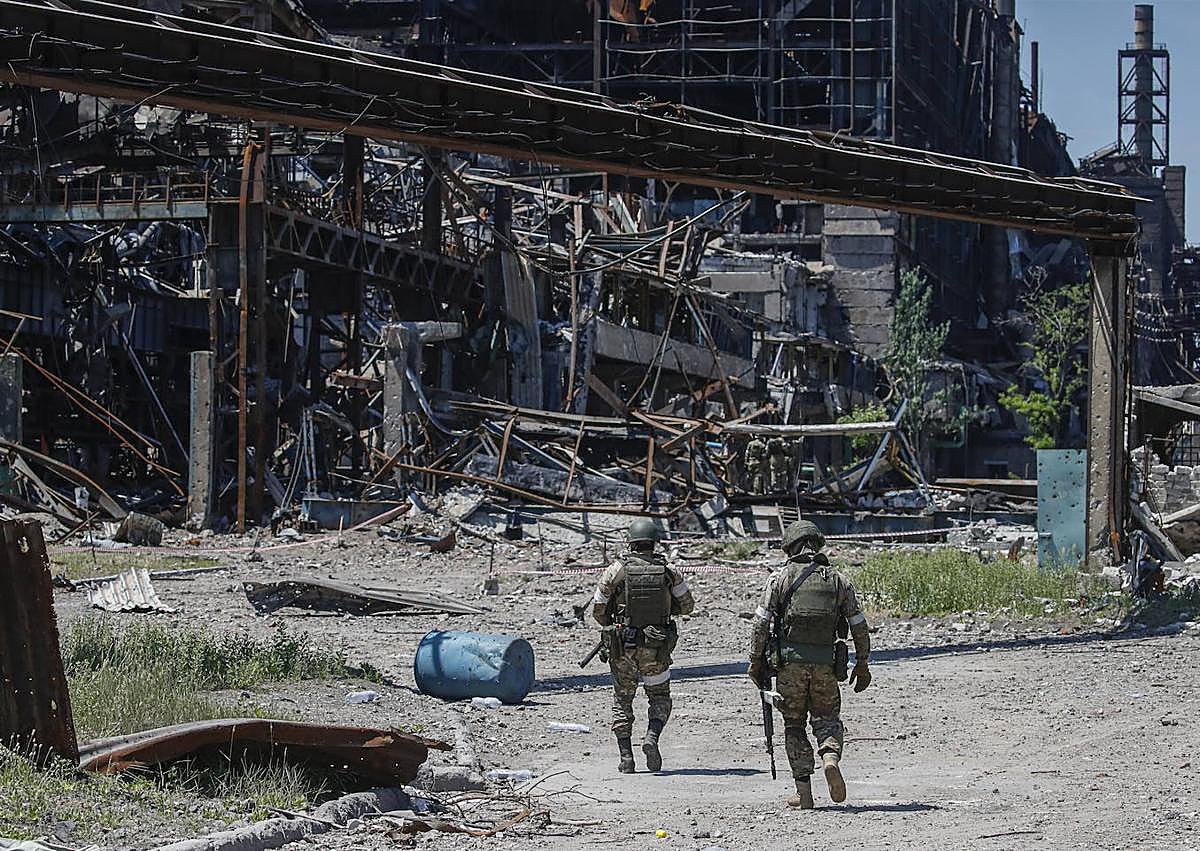 Imagen secundaria 1 - Una bomba estalla durante el asedio ruso a la planta. Dos Soldados caminan sobre el entramado de hierros en el que se convirtió la acería tras los ataques.