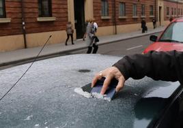 Una mujer limpia el hielo de su coche por el intenso frio en Valladolid