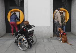 Varias personas hacen gestiones bancarias en dos cajeros automáticos.