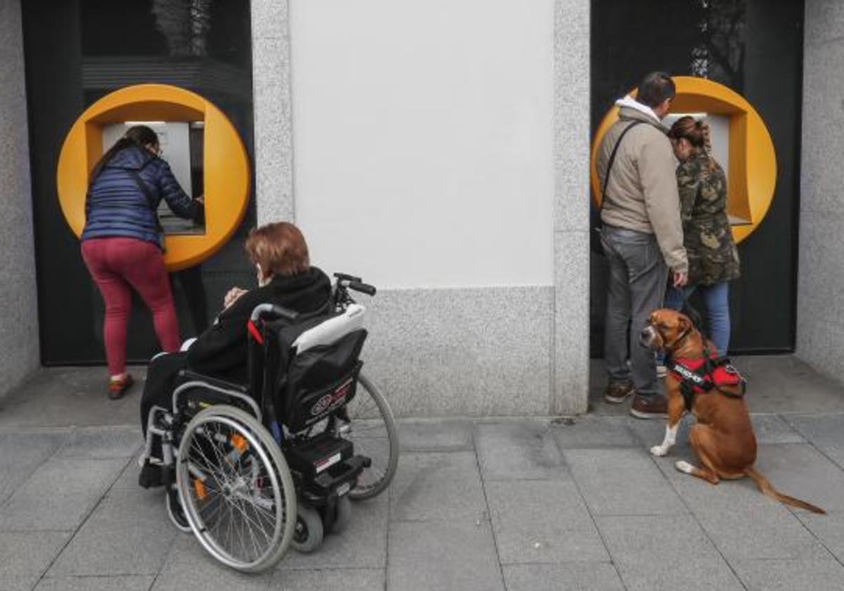 Varias personas hacen gestiones bancarias en dos cajeros automáticos.