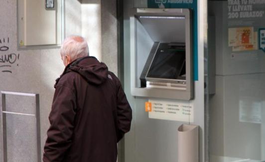 Una persona mayor pasa junto a un cajero automático. 