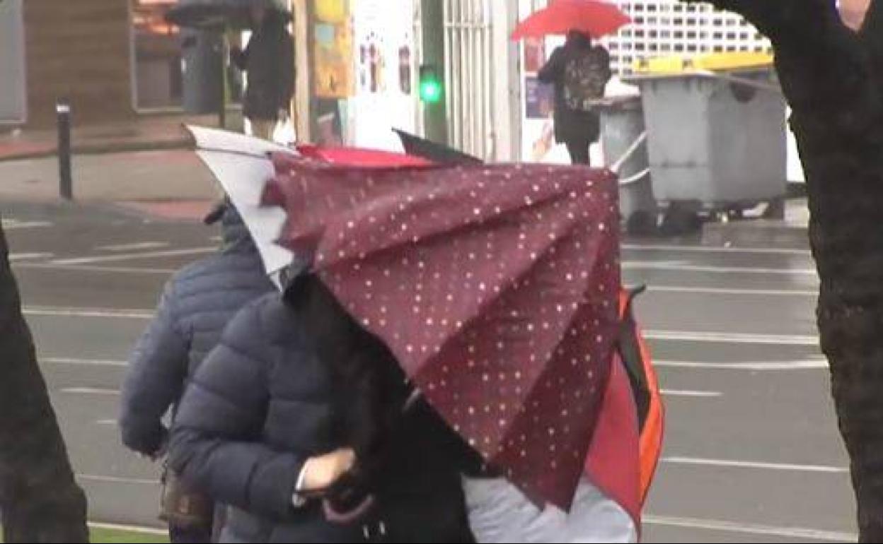 Viandantes con parajuas pelgados por el viento en Burgos. 