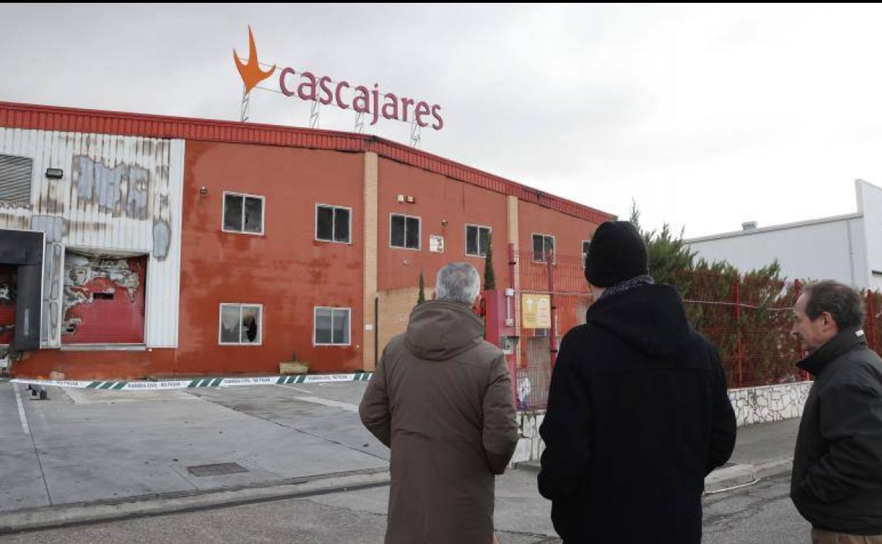 Tres hombres contemplan desde el exterior la fábrica quemada.