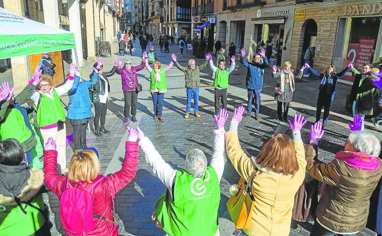 Miembros de la asociación y representantes institucionales forman un lazo humano con las manos pintadas de morado en la Calle Mayor.