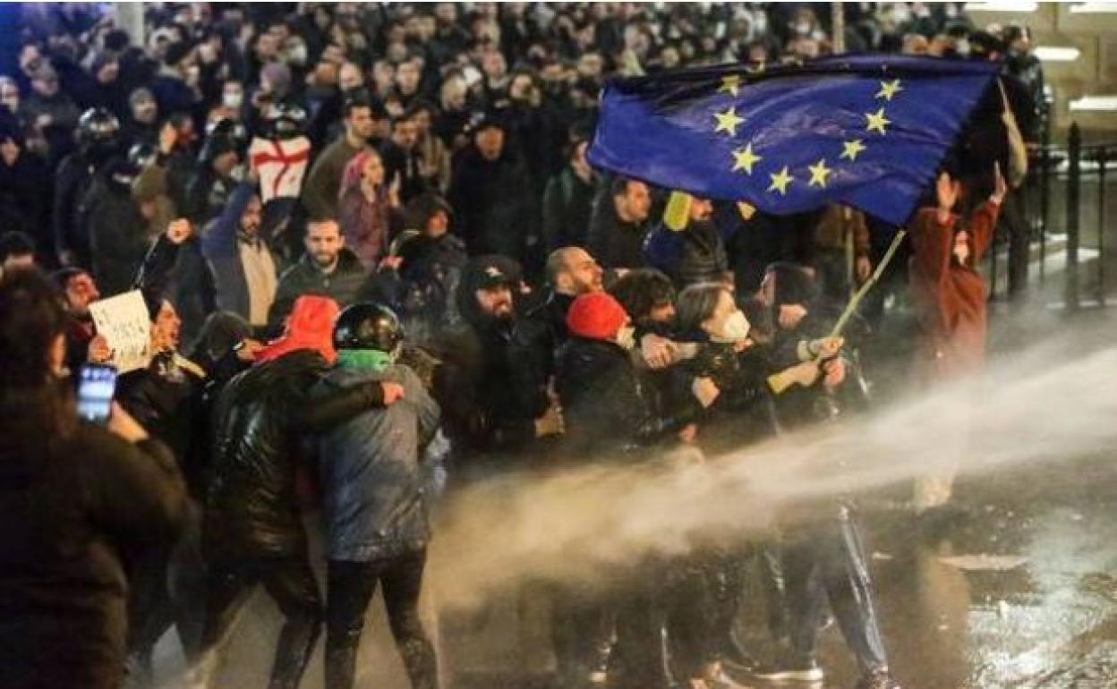 Manifestantes con una bandera de la Unión Europea son rociados por un cañón de agua durante las protestas en Georgia.