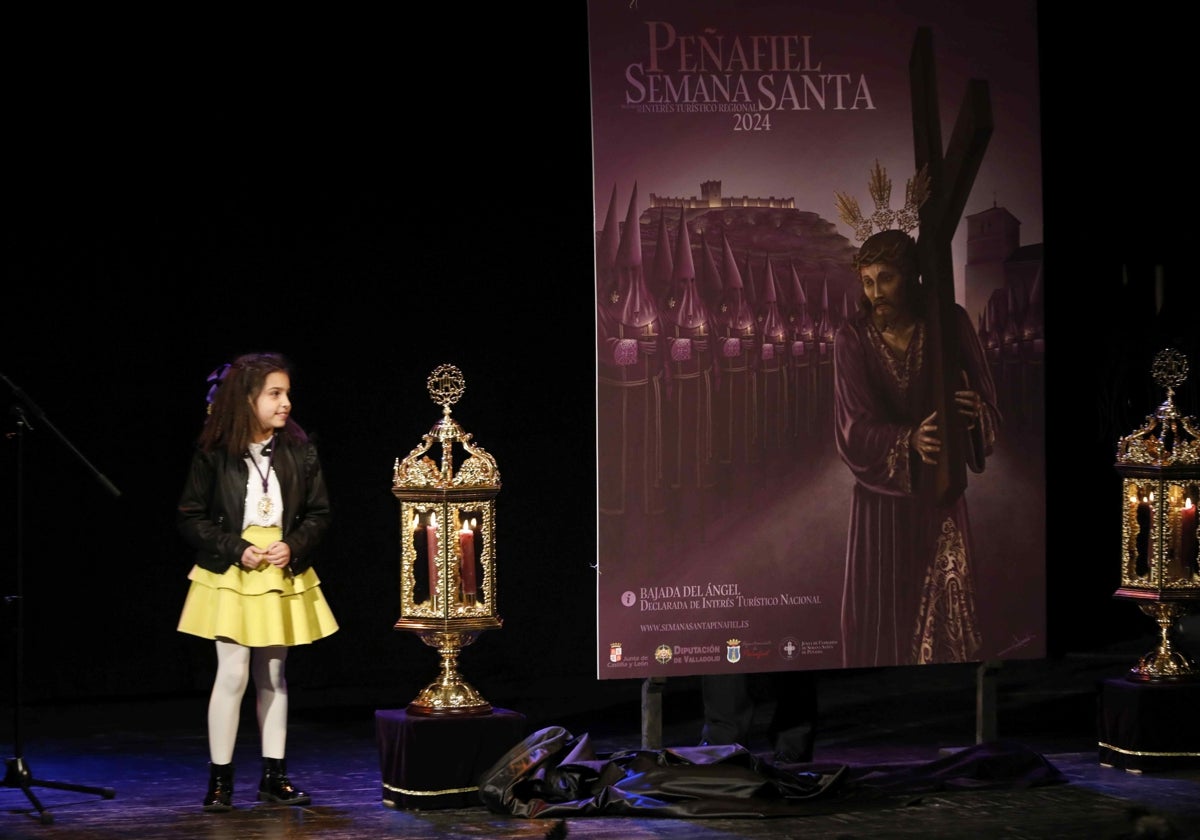 Julia Soria González, niña que protagonizará la Bajada del Ángel el Domingo de Resurrección, junto al cartel de la Semana Santa de Peñafiel.