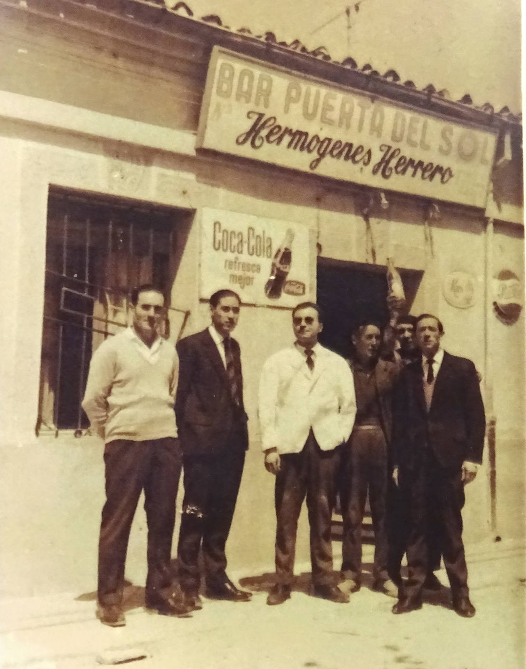 Imagen secundaria 2 - Arriba, los hermanos Herrero del Moral, Julio y Luis, con un trabajador de la cantina y Julio, hijo de Julio y nieto de Hermógenes. Abajo, Julio Herrero, ante la puerta del negocio Bodegas Hermógenes, en el 190 del Paseo de Zorrilla. A la derecha, Hermógenes Herrero junto a varios clientes a la puerta de la Puerta del Sol.