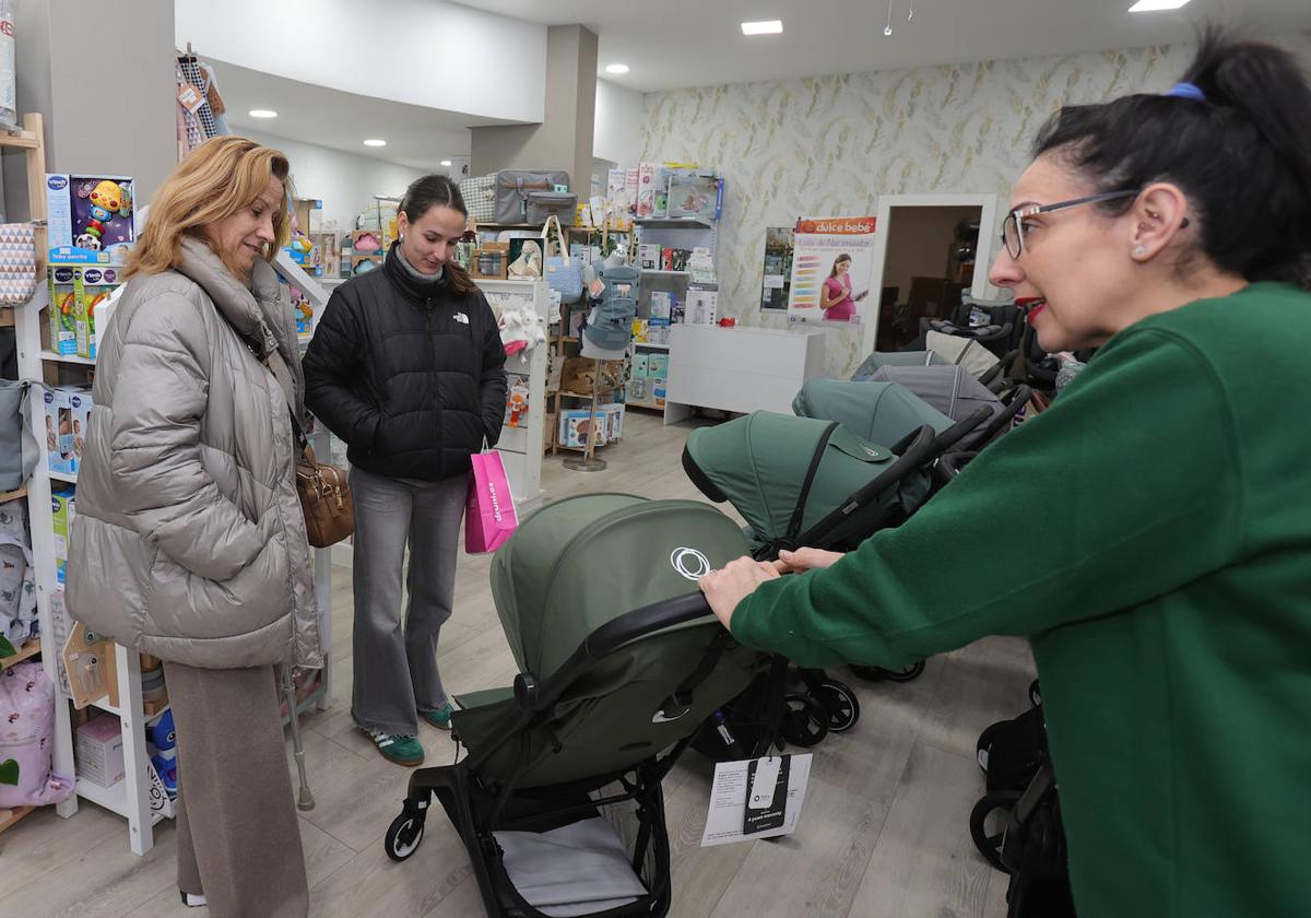 Una dependienta de la tienda Dulce Bebé muestra sillas de paseo a dos clientas.