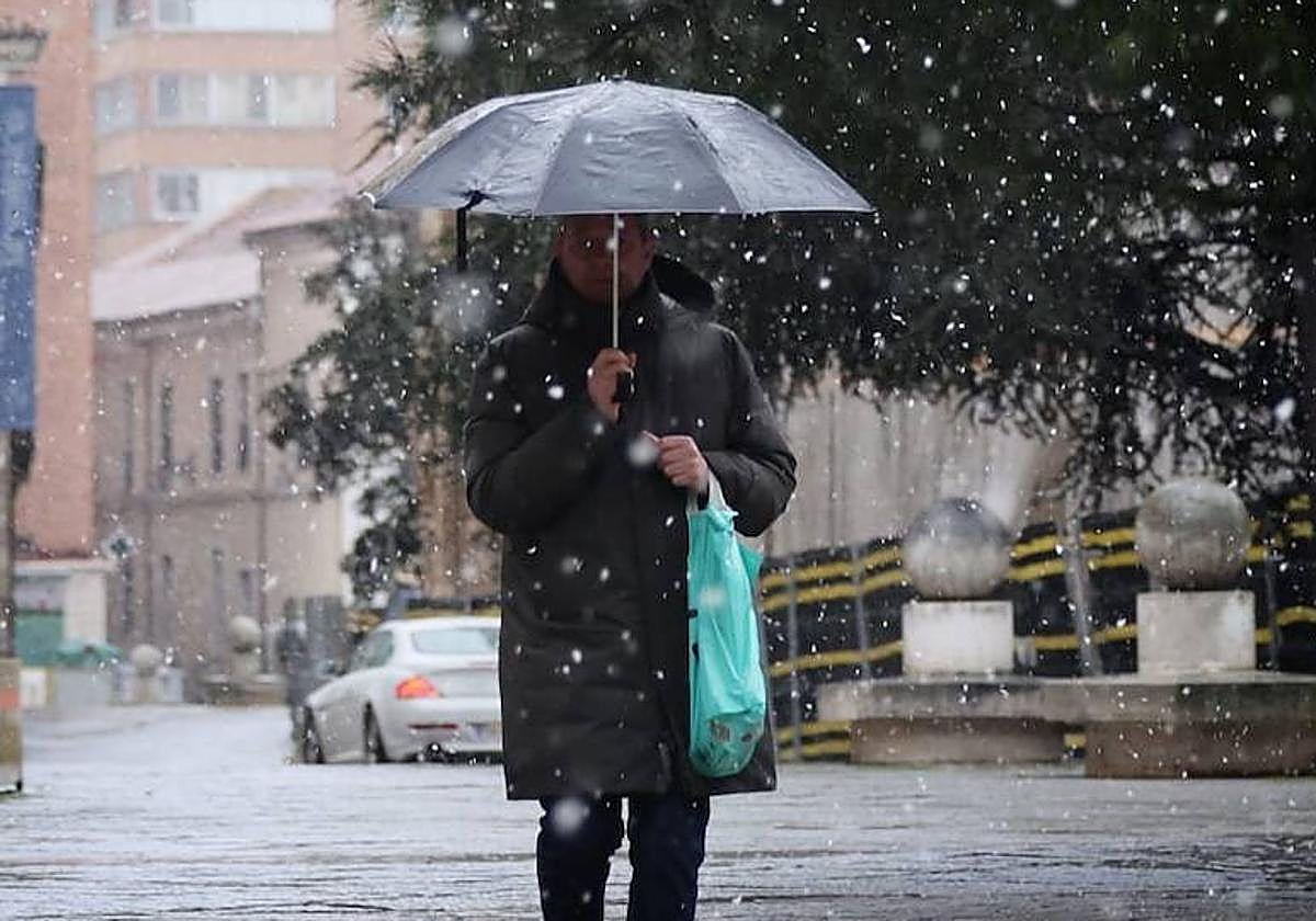 Un viandante se protege bajo un paraguas de la primera nevada del año en Valladolid.