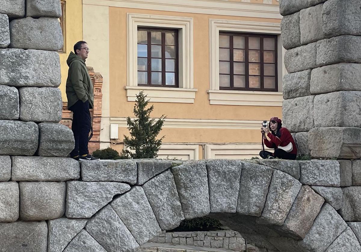 Dos turistas asiáticos realizan fotografías subidos en los sillares del Acueducto, en el tramo de la plaza de Día Sanz.