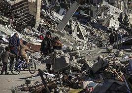 La gente camina junto a las ruinas de los edificios destruidos por los bombardeos israelíes en el campo de refugiados de Jabalia.