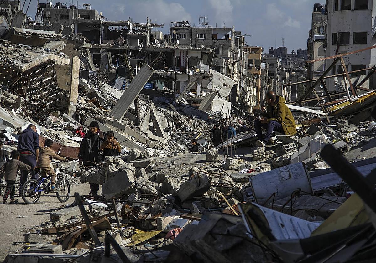 La gente camina junto a las ruinas de los edificios destruidos por los bombardeos israelíes en el campo de refugiados de Jabalia.
