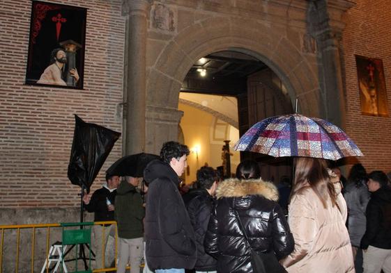 Varias personas, tapadas con paraguas en la puerta de la iglesia tras la suspensión de la Procesión de la Caridad.