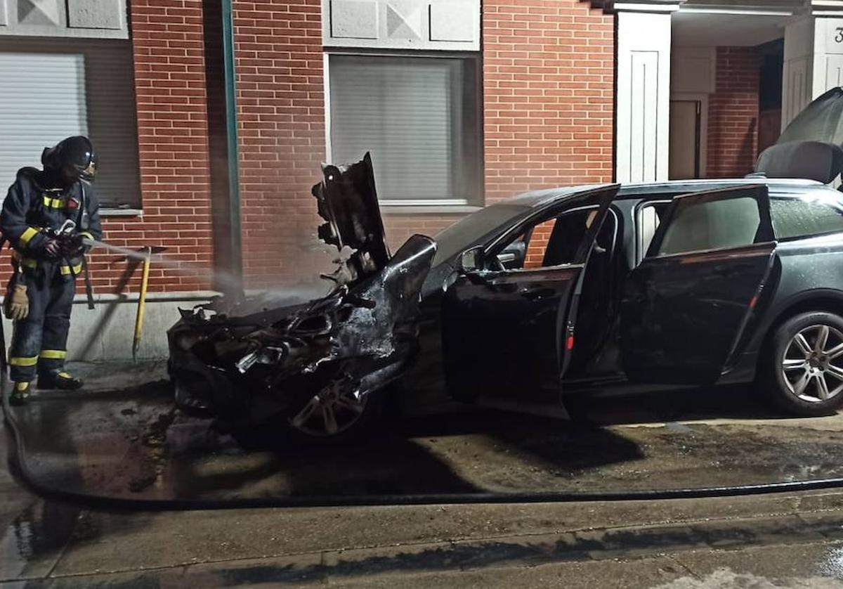 Un bombero sofoca el incendio en uno de los coches dañados.