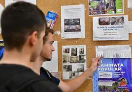 Dos jóvenes miran un panel donde se anuncian alquileres para estudiantes en Valladolid.