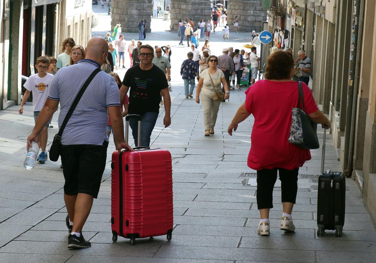 Dos personas pasean con maletas por el centro de la ciudad de Segovia.