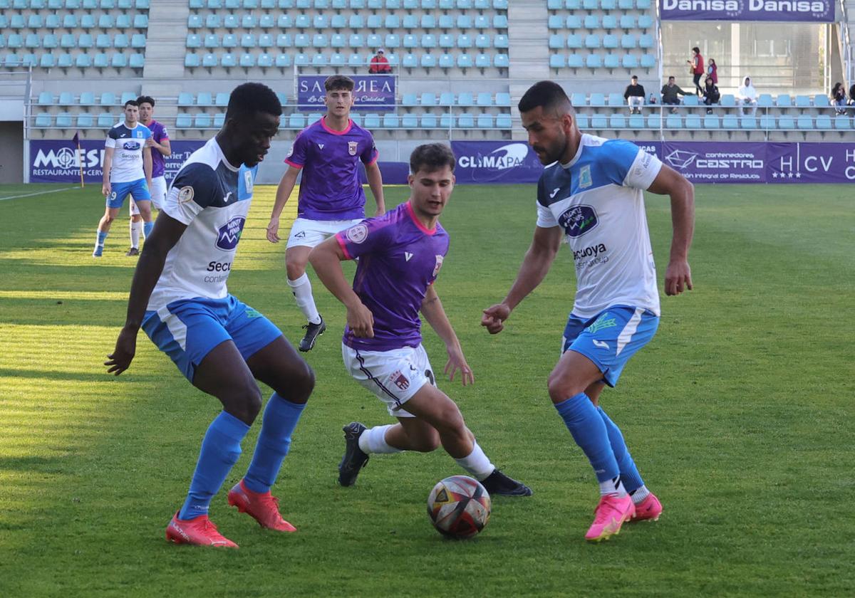 Mario Vallejo intenta llevarse el balón entre dos rivales en el partido entre el Palencia CFy el Almazán en La Balastera.