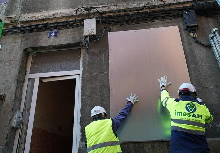 Dos operarios colocan una chapa metálica en una de las ventanas del número 4 de la calle Olmedo.