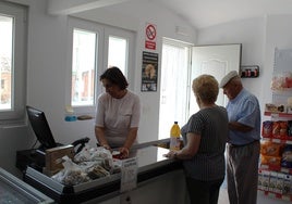 Olga Sánchez atendiendo a dos clientes en la tienda de alimentación