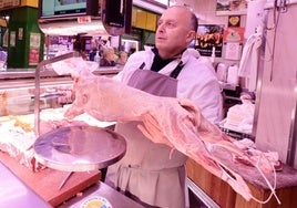 Un carnicero con un lechazo en su puesto del Mercado del Campillo de Valladolid.