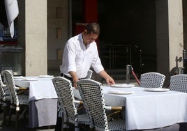 Un trabajador hostelero prepara una mesa en una terraza.