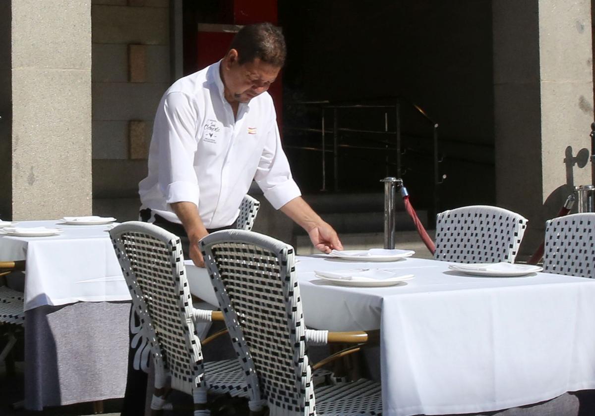 Un trabajador hostelero prepara una mesa en una terraza.