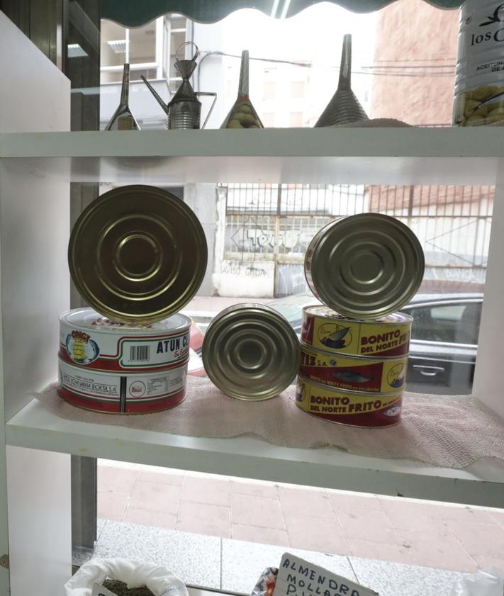 Imagen secundaria 2 - Fachada de la tienda de Hijos de Faustino Hernández en la calle Sevilla, conservas en los estantes y la vista de la calle desde el interior.