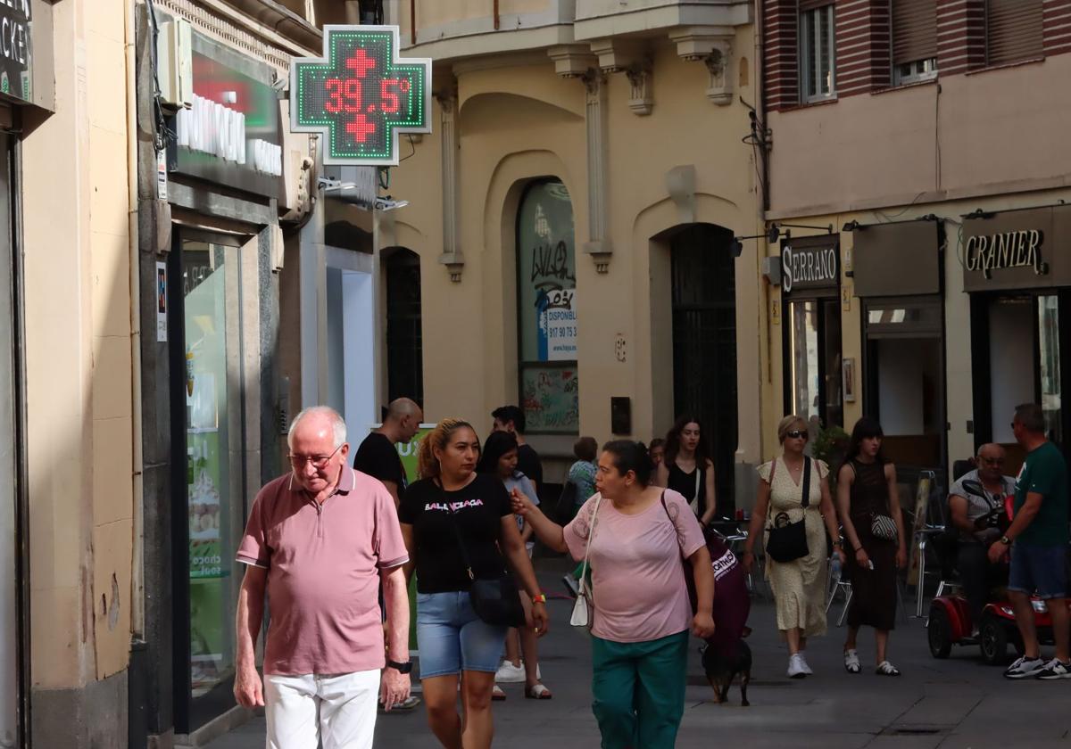 Traseúntes pasean este lunes por la Calle Real ante un termómetro que marca 39,5 grados.