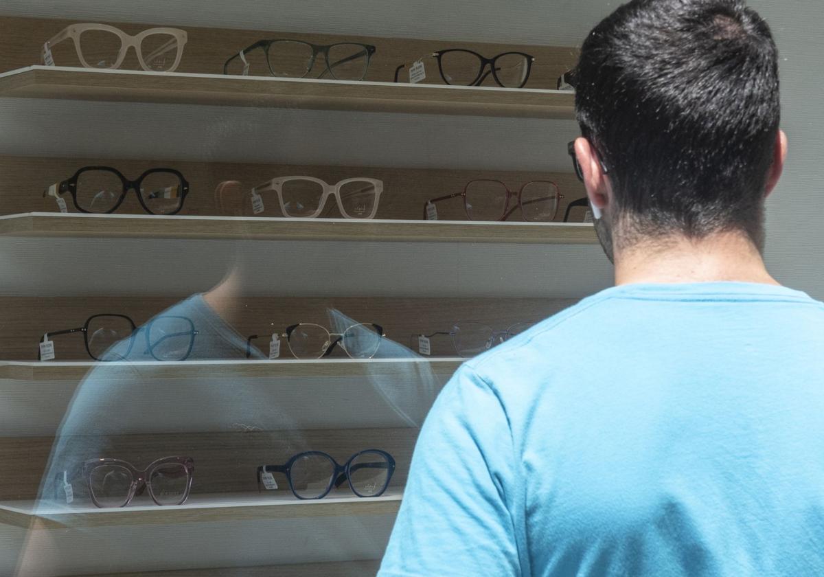 Un hombre observa varias gafas en el escaparate de una óptica de Segovia.