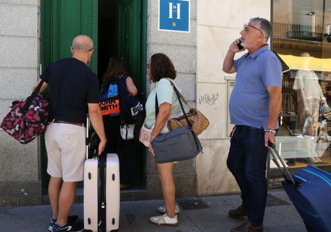 Varias personas esperan con sus maletas a la puerta de un hotel.