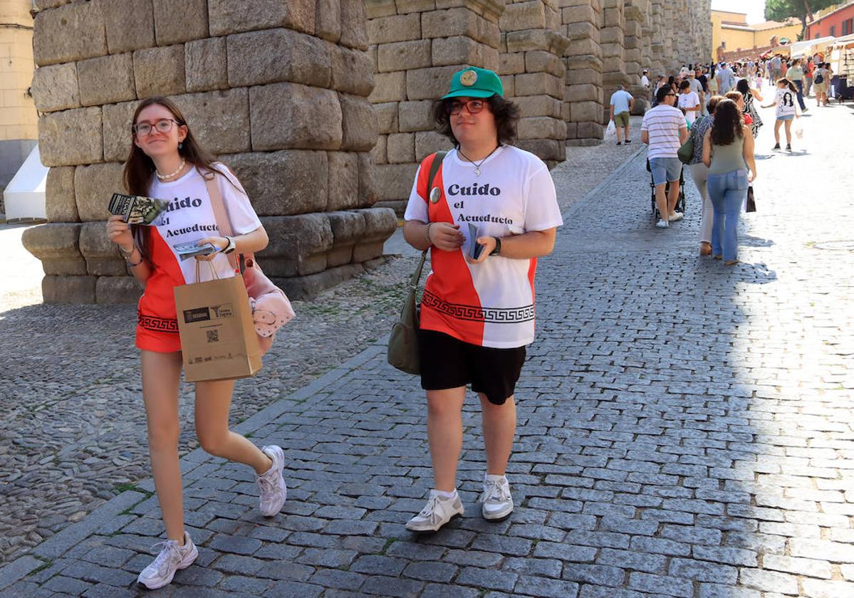 Dos de los voluntarios descienden por la calle Teodosio el Grande repartiendo marcapáginas.