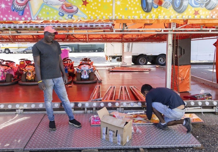 Dos operarios trabajan en el montaje de la pista de motos infantil en el Real de la Feria.