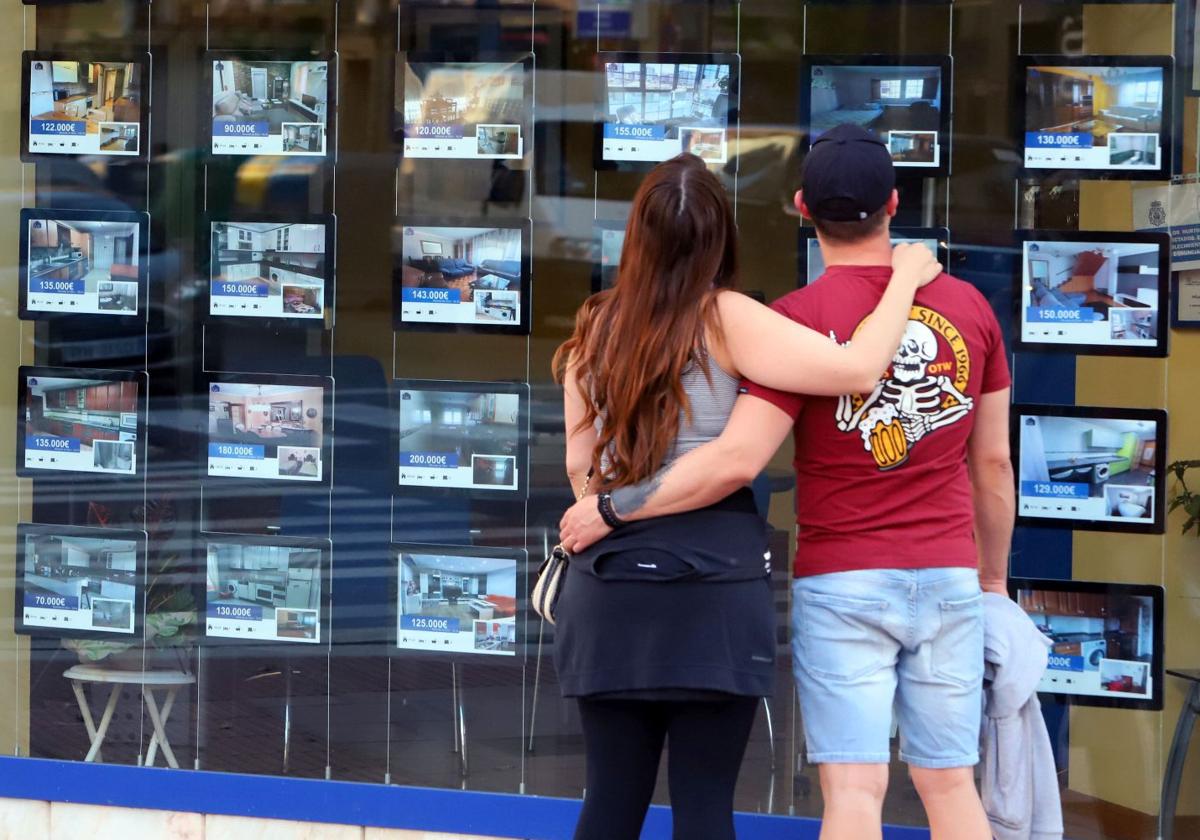 Una pareja de jóvenes mira el escaparate de una inmobiliaria en Miranda de Ebro.