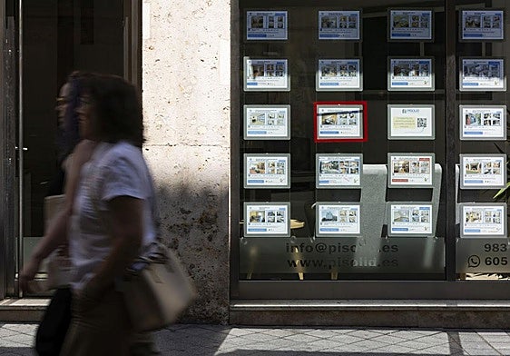 Varios peatones pasan delante de una céntrica inmobiliaria de Valladolid.