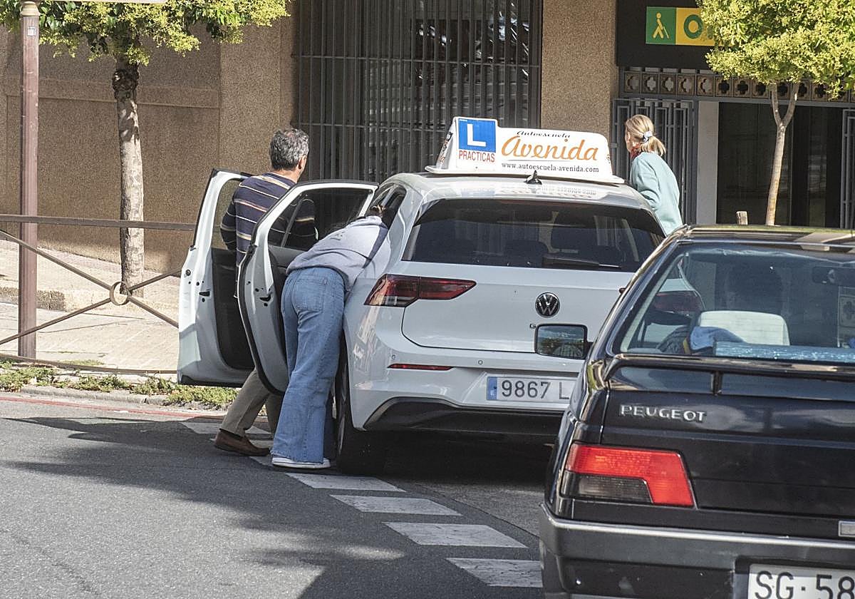 Una alumna se sube a un coche de autoescuela junto a su profesor.