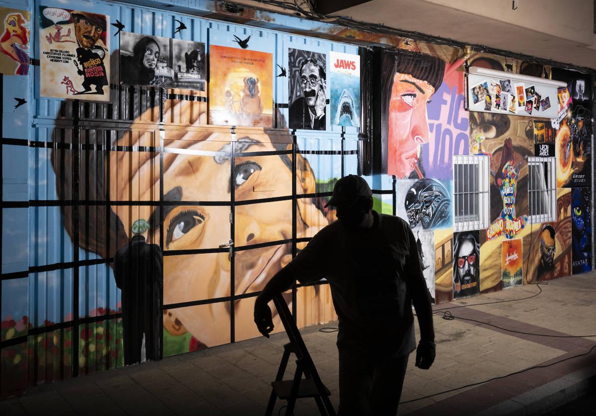 El artista R., junto al mural dedicado al cine que ha pintado en la calle Penitencia.
