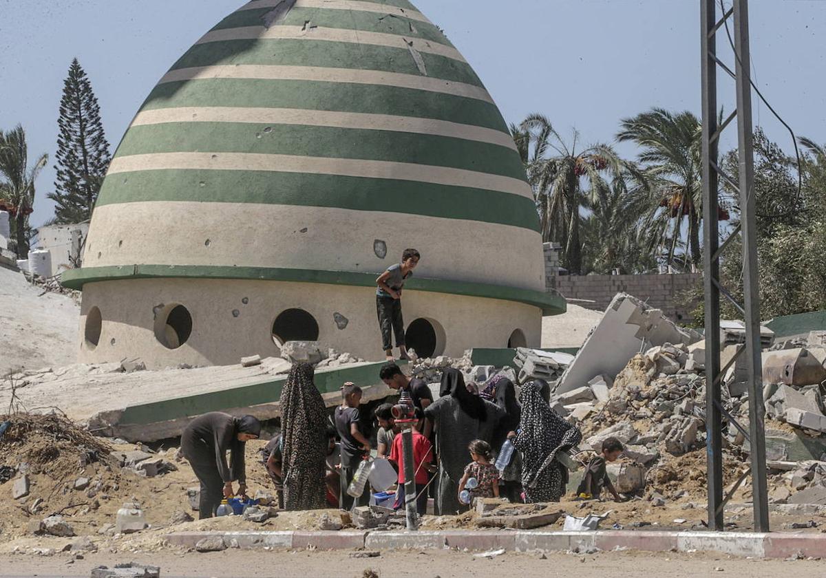 Palestinos desplazados esperan para llenar el tanque de agua cerca de edificios destruidos en Deir Al Balah, en el centro de la Franja de Gaza.