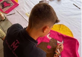 Un niño pinta un toro en su capote durante el taller