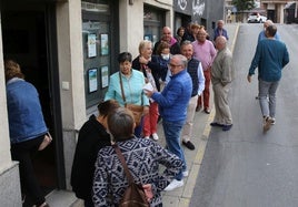 Varias personas esperan en una cola a las puertas de una agencia de viajes.