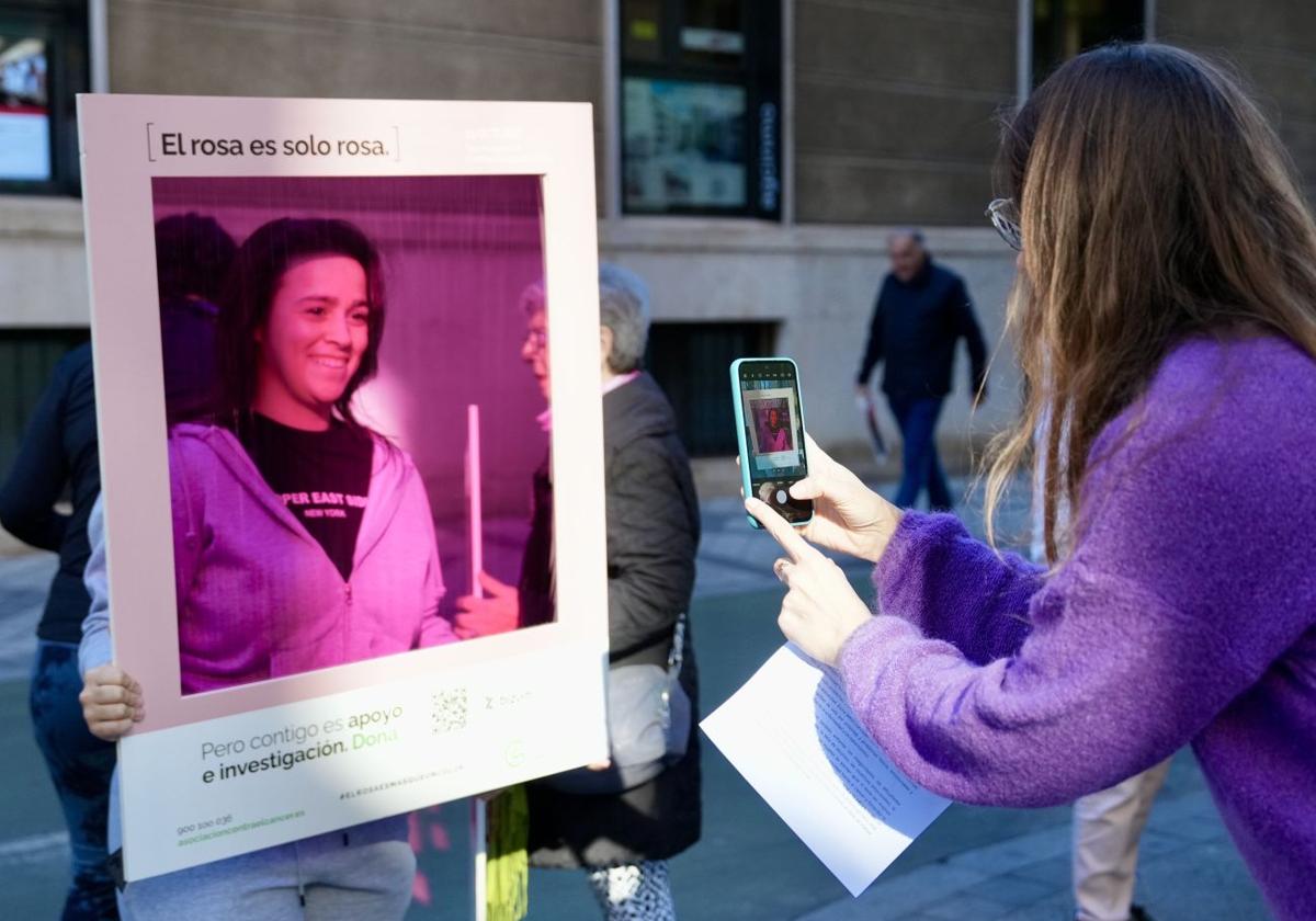 Una mujer posa con el marco rosa de la campaña para reclamar investigación contra el cáncer de mama.