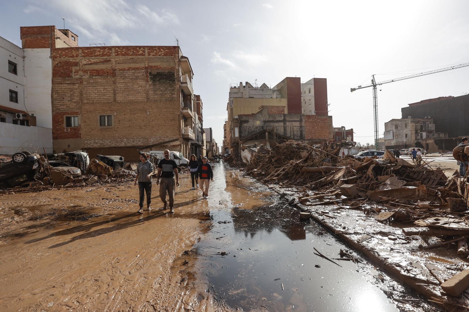 Varias personas caminan entre los destrozos causados por las intensas lluvias caídas por la fuerte dana, este jueves en Catarroja.