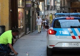 Un coche de la Policía Local pasa junto a un hombre que pide limosna en la Calle Real.