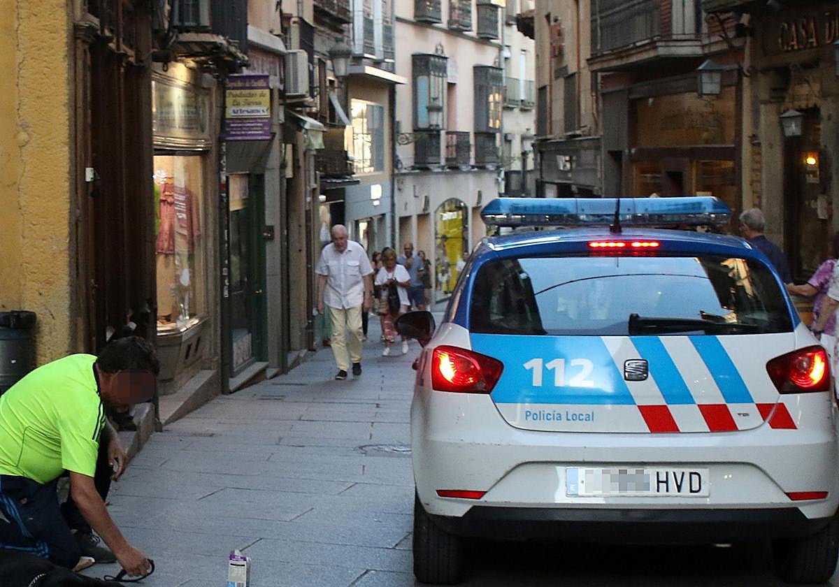 Un coche de la Policía Local pasa junto a un hombre que pide limosna en la Calle Real.