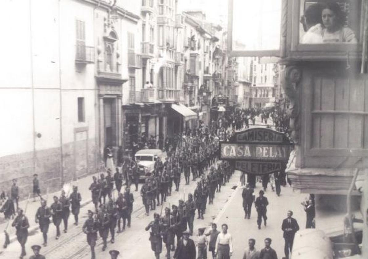 Una mujer, asomada a la ventana, mientras las tropas desfilan por la calle Santiago.