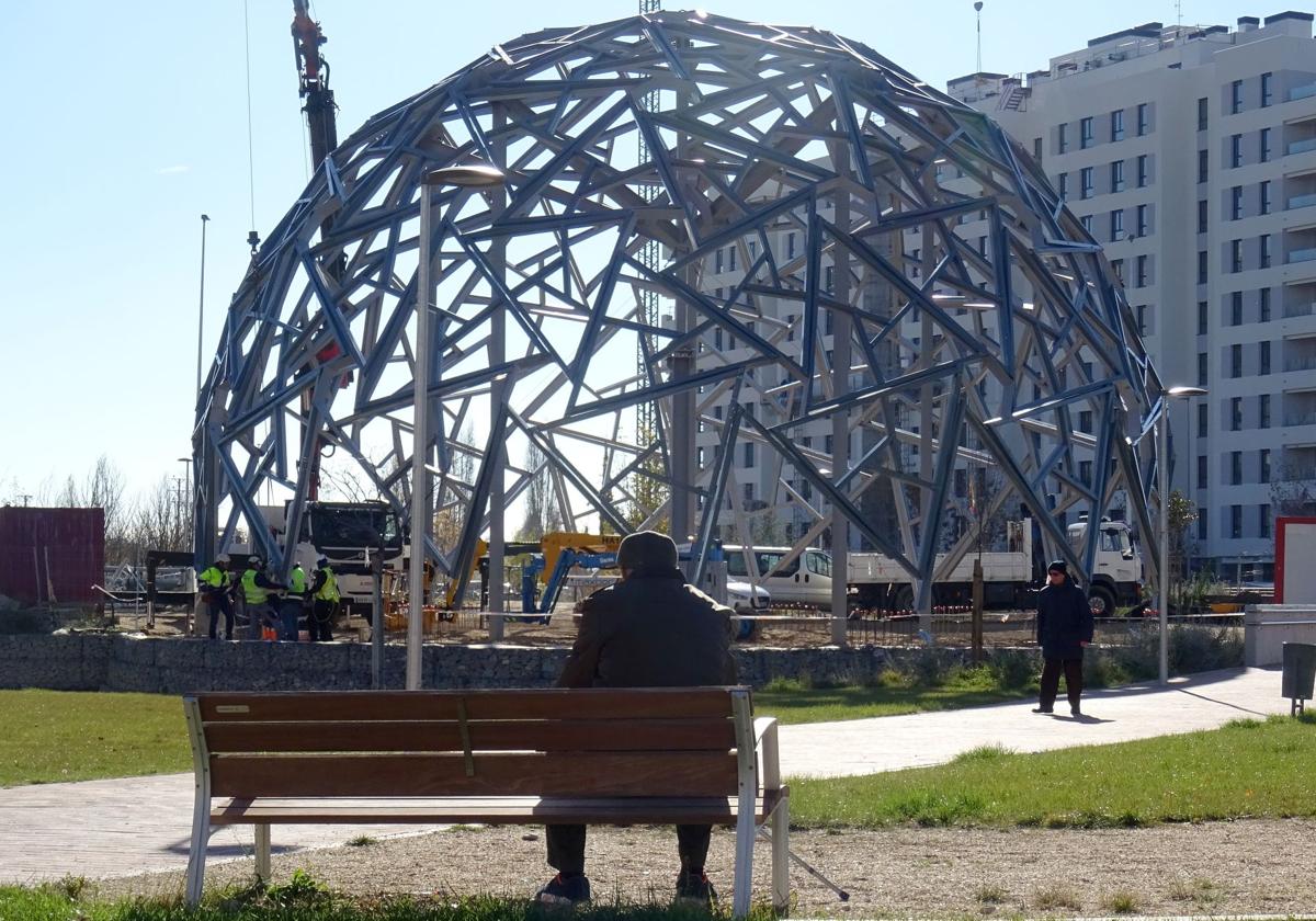 Un hombre observa la geoda mientras los operarios rematan el último anillo a ras de suelo en la plaza de la Ciudad de la Comunicación.