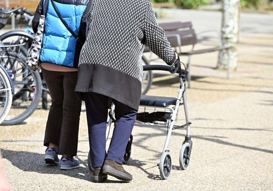 Una anciana pasea apoyada en un andador y con la ayuda de una acompañante