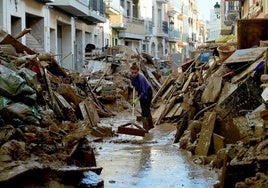 Una mujer limpia el barro en una calle de Paiporta entre las montañas de escombros que dejaron las mortíferas inundaciones.